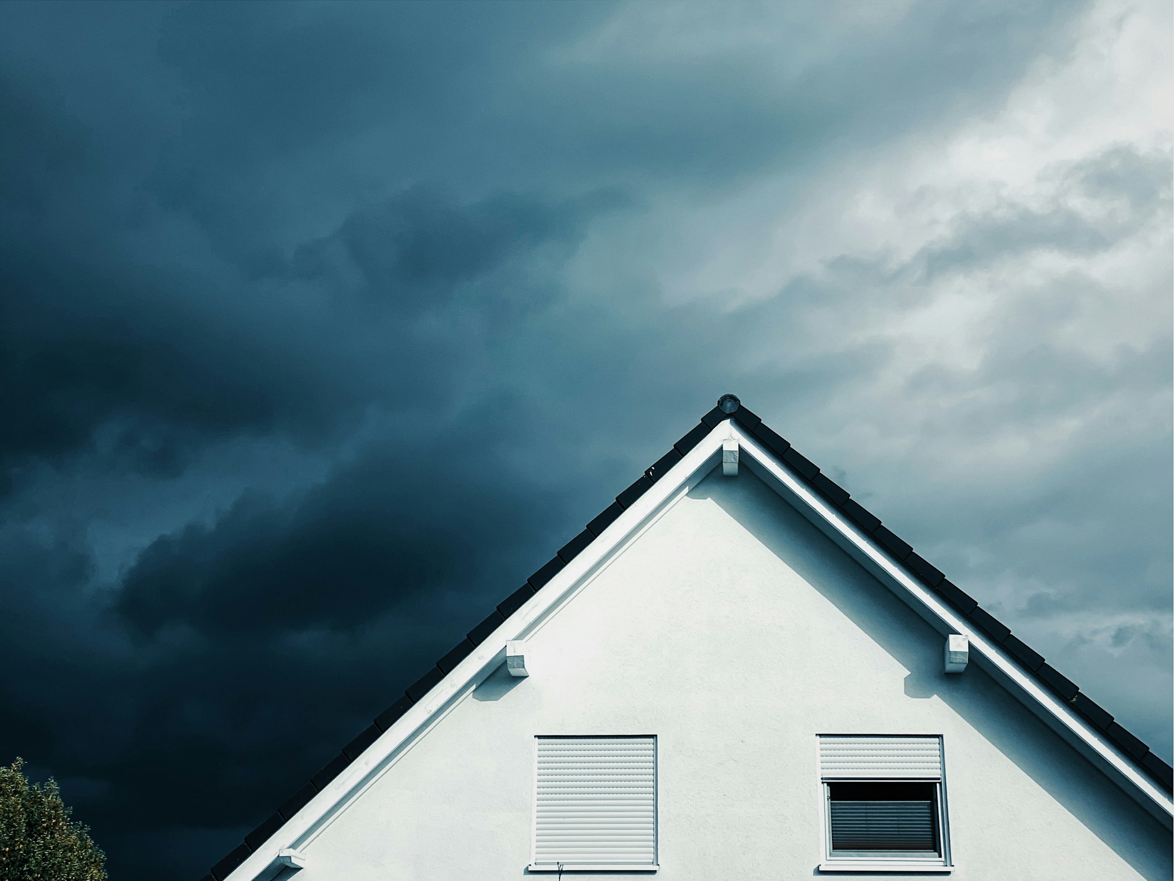The white gable of a house with a dark roof edge against heavy blue-grey storm clouds