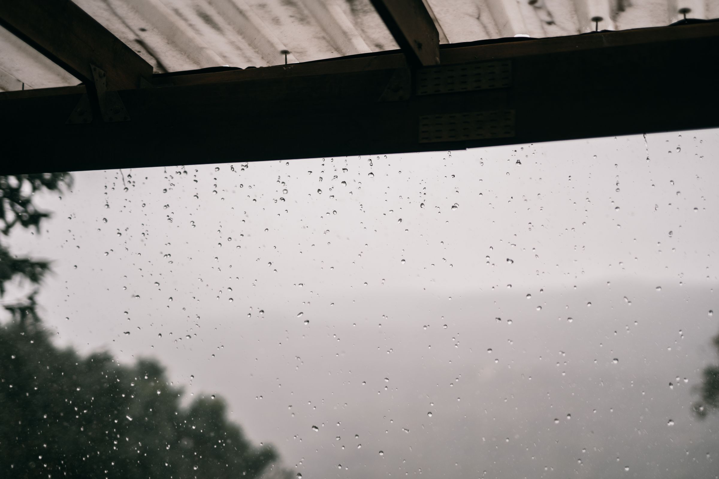 Rain dripping from the edge of a roof, with trees blurred in the grey background